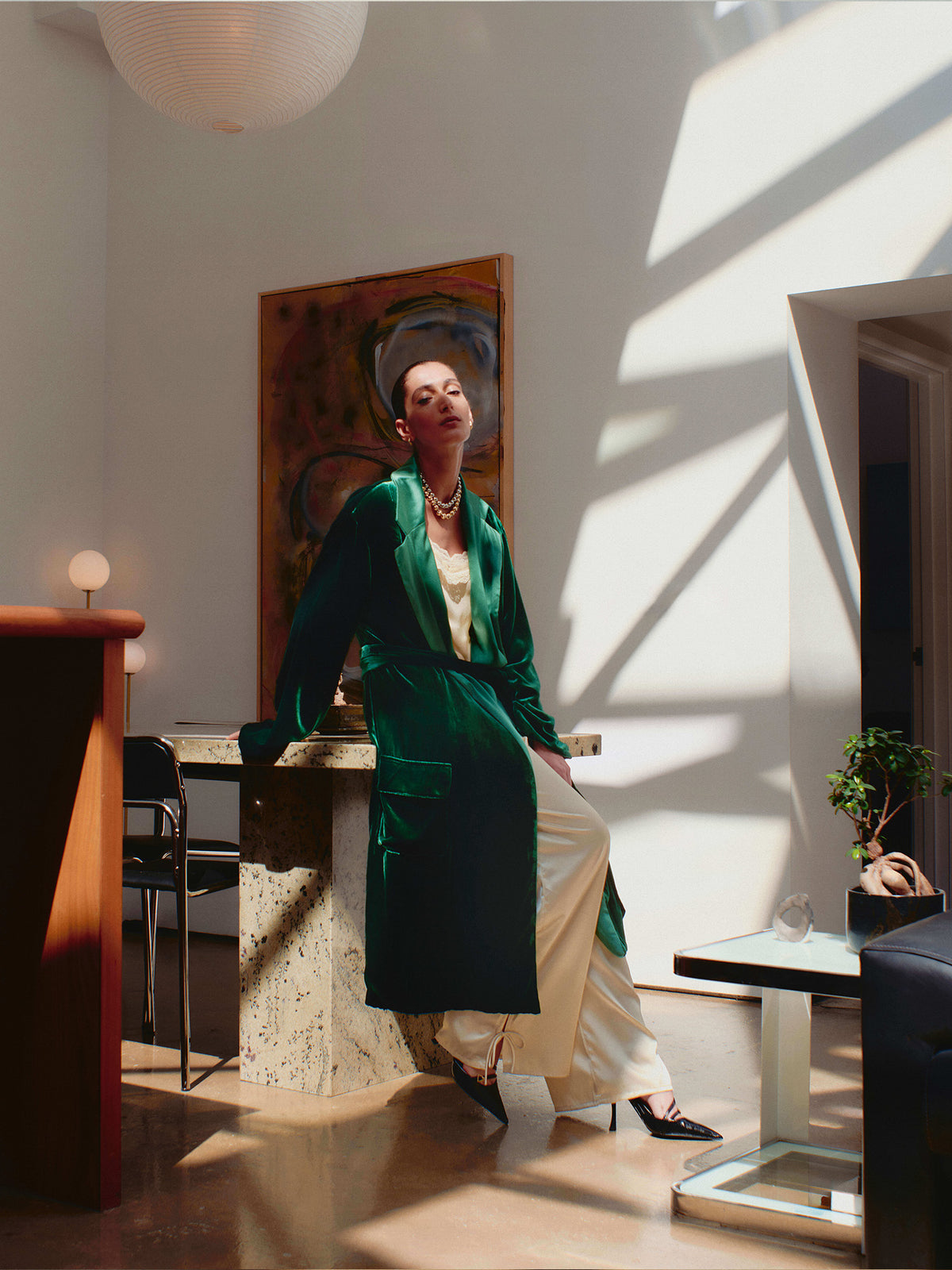 Model wearing the dark green velvet Reversible Robe over cream wide-leg trousers and black pointed heels
